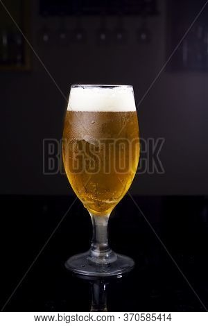 Ice Cold Glass Full Of Beer, With Chopp Pilsen On A Dark Background In A Pub