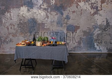 Stand-up meal with tasty food and drinks on tablecloth. Table placed in an industial interior with textured wall with copy space