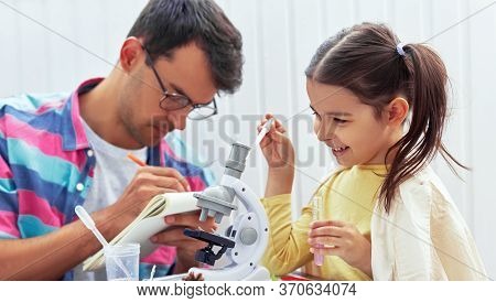 Happy Child Doing Science Experiments In The Laboratory Together With Her Father Who Makes Notices O
