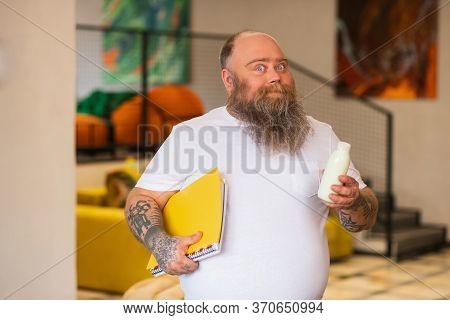 Bald Bearded Plump Manstanding And Holding A Bottle With Milk