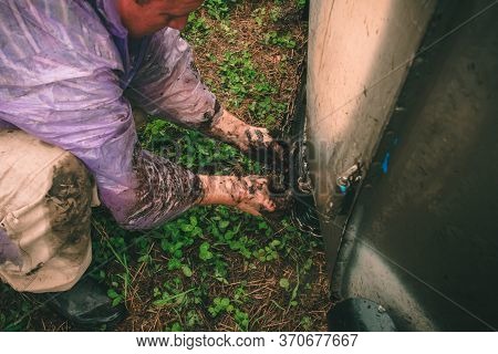 A Man With Muddy Hands Puts Chains On The Wheels Of A Car To Avoid Slipping And Skidding, To Drive T
