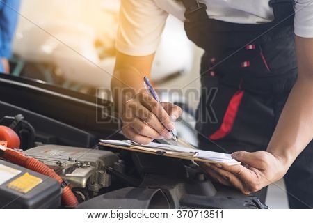 Auto Check Up And Car Service Shop Concept. Mechanic Writing Job Checklist To Clipboard To Estimate 
