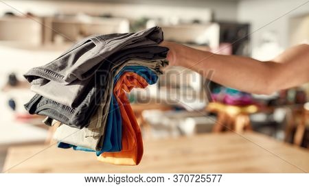 Cropped Shot Of Hand Of Woman Holding Stack Of Colorful T Shirts While Standing In The Store. Clothe