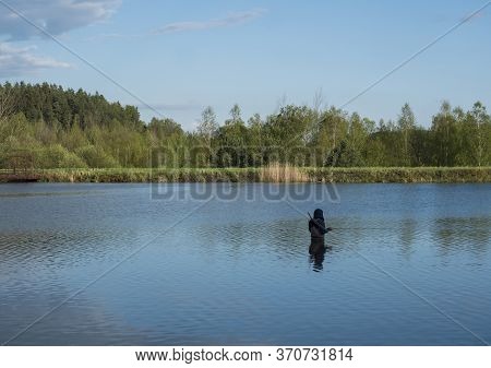 Fly Fisherman Angler Standing In Calm Water Of Forest Lake, Fish Pond Kunraticky Rybnik With Birch A