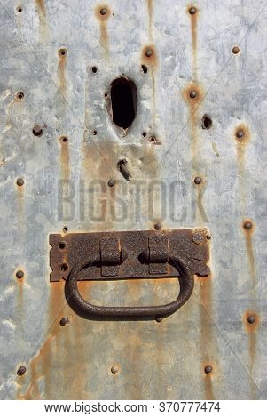 rusty handle and keyhole on old door coated with nailed galvanized sheet metal in Sicily