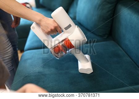 Close-up Of Womans Hand Cleaning Green Sofa With Small White Electrical Compact Vacuum Cleaner. Styl