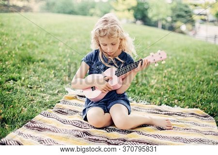 Cute Adorable Blonde Girl Playing Pink Guitar Toy Outdoor. Child Playing Music And Singing Song In P