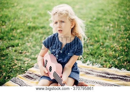 Cute Adorable Blonde Girl Playing Pink Guitar Toy Outdoor. Child Playing Music And Singing Song In P