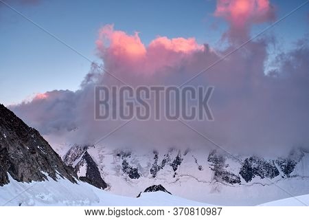 Sunset In Mountains. Reflection Of Red Sun On Mountain Snow Peaks And Clouds. Altai, Belukha Area