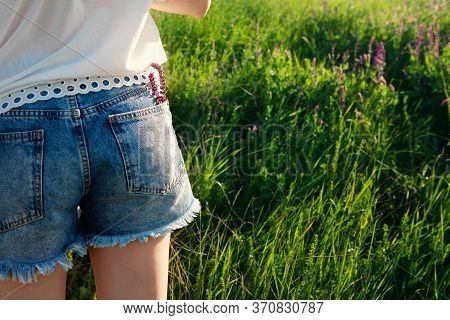 Young Woman With Flowers In Jeans Short Pocket On Meadow Background