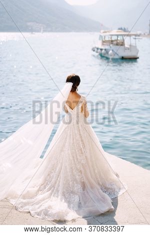 The Bride Stands On The Pier Of The City Of Perast In Montenegro, And Admires The Mountains And Moor