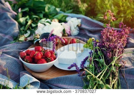 Picnic In Grass, Cheese, Strawberries, Wildflowers On Wooden Board.