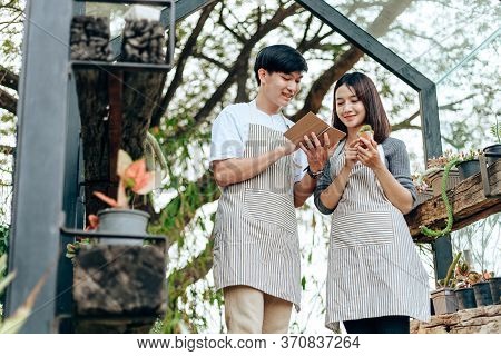 Women Hold Cactus And A Man Writing Note In A Book. Love Couple Enjoy Hobby With Darden Cactus.