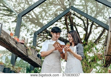 Women Hold Cactus And A Man Writing Note In A Book. Love Couple Enjoy Hobby With Darden Cactus.
