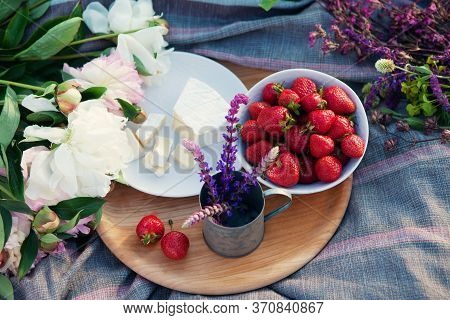 Picnic In Grass, Cheese, Strawberries, Wildflowers On Wooden Board.