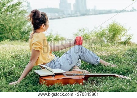 Hands Hold Coffee Cup And Write Notes,lyrics In The Book On Quitar Beside The Sea And Building City 
