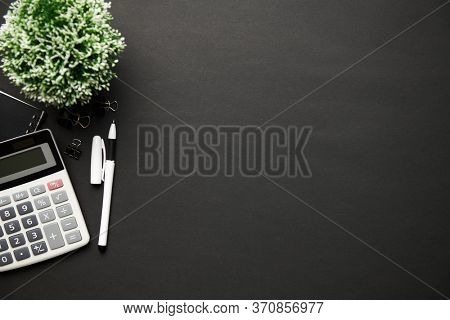 Top view of modern black office desk with calc, notebook, pen and a lot of things. Flat lay table layout. Copy space for text.