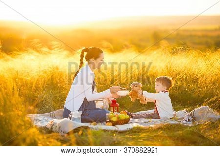 Cute Mom And Little Son Playing With My Teddy. Mother And Son Feeding Teddy Bear On A Picnic