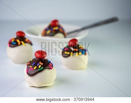 Banana Split Cake Balls With White Coating, Chocolate Drizzle Covered In Sprinkles And A Cherry On T