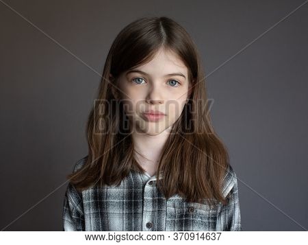 Portrait Of A Little Beautiful Brunette Girl With Long Hair In A Plaid Shirt On A Gray Background