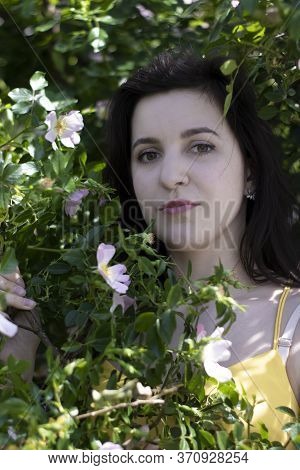 Attractive Young Brunette Woman In Yellow T-shirt. In A Bush Full Of Floweers. Copy Space.