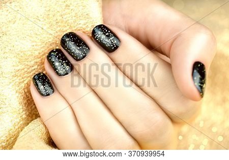 Female Hand With Black Manicure And Gold Sparkles On A Golden Background