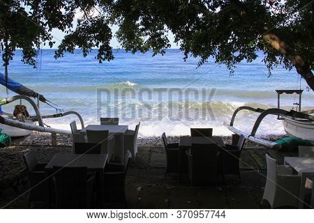 Empty Terrace With No Tourists And Jukung Boats On Sunny Day In Bali, Indonesia. Tables And Chairs A