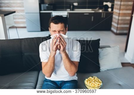 Young Man Watch Tv In His Own Apartment. Guy Sneezing Into White Napkin. Sick And Ill At Home. Suffe