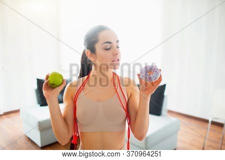 Young Woman Doing Yoga Workout In Room During Quarantine. Choosing Between Fatning Burger And Health