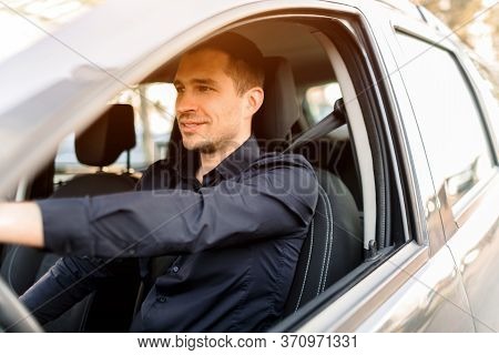 A Young Man In A Dark Shirt Driving His Own Car. Positive And Confident Taxi Driver