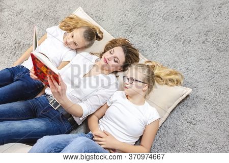 Family Ideas. Portrait Of Caucasian Mother Reading A Book Together With Her Female Twins Laying On F