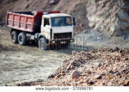 Selective Focus Pile Of Ore Rocks Over Background With Heavy Laden Multi-ton Truck Exporting Mineral