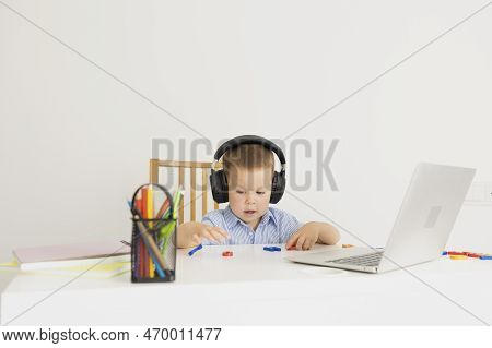 A Little Boy In Headphones Makes Uraki And Completes Tasks. At A White Table, A Schoolboy Sits In Fr