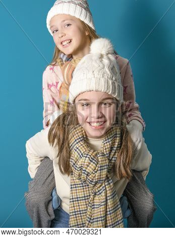 Two Sisters Or Teenage Friends Play Leapfrog. Winter Motif And Clothes. Studio Photo. Sweaters, Scar