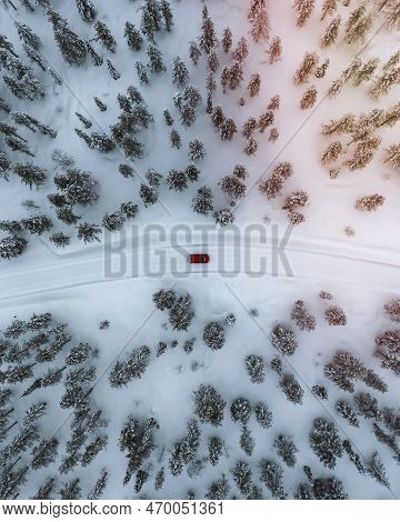 Drone View Of A Red Car Driving Though A Snowy Forest In Lapland, Finland