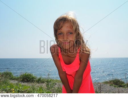 A Young Pretty Girl Of 8 Years Old With Blond Long Hair, Tanned Skin Smiles Against The Backdrop Of 
