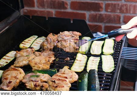 Hand Holding Piece Of Grilled Meat While Grilling Chicken And Zukini Vegetables On Outdoor Barbecue 