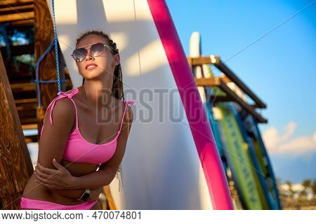 Young Fashionable Girl Of An Athletic Build In A Pink Bikini Poses Against The Background Of A Sap S
