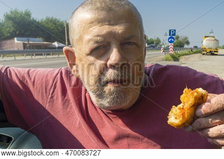 Portrait Of Hungry Ukrainian Senior Driver Taking Patty Near His Car While Standing Near Vasylivka, 
