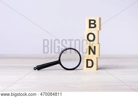 Magnifying Glass And Wooden Blocks With Text Bond On Wood Table, Grey Background