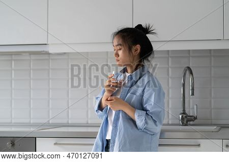 Weakened Lonely Asian Woman Standing In Kitchen Of Own Home With Glass With Eyes Closed. Young Chine