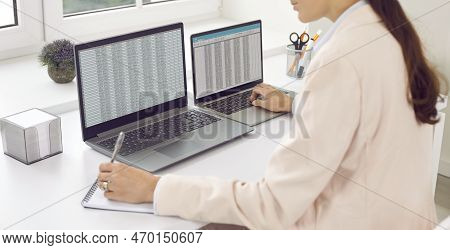 Attractive Young Woman Is Sitting In Office At Workplace At Desk With Laptop. Girl Makes Audit, Acco