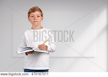 Pondering Handsome Boy In Casual Wear Standing Holding Notebook And Taking Notes Near Empty White Wa