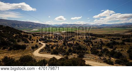 Backcountry Nature Panorama Of Road Winding Through Dry Rural Landscape And Green Agriculture Fields