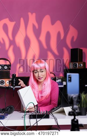 Content Creator With Pink Hair Holding White Box Presenting Product In Front Of Phone Camera, Filmin