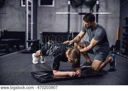 A Woman In A Black Ems Training Suit Laying In A Plank Position On Her Elbows In The Middle Of A Tra