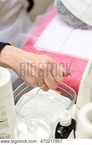 A Close-up Of A Beautician's Hand Squeezes Water Out Of A Cotton Ball.