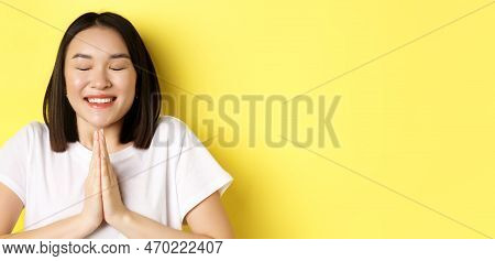Close Up Of Hopeful Asian Girl In White T-shirt, Holding Hands In Pray, Namste Gesture And Smiling, 