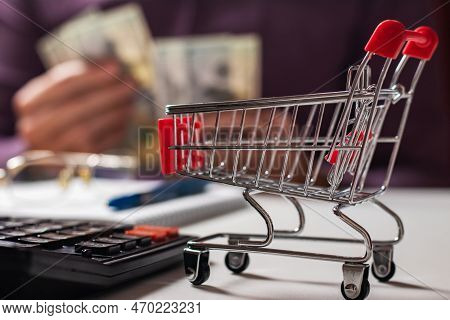 Man Calculates The Budget. Shopping Cart A On Table With Calculator And Paper And Mohey In Hadns. Bu