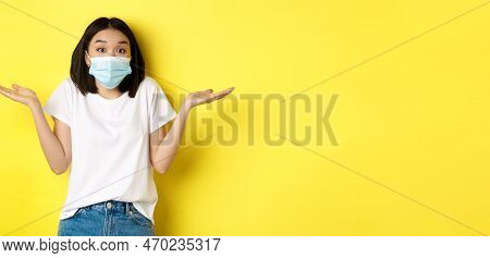 Covid-19, Quarantine And Social Distancing Concept. Clueless Asian Woman In Medical Mask Shrugging S